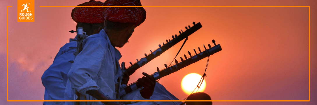 2 Indian men sitting with instruments with sunset in the background